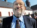 Porträt eines älteren Mannes mit Brille, Schnurrbart und Bart, der einen Anzug und eine Krawatte trägt.