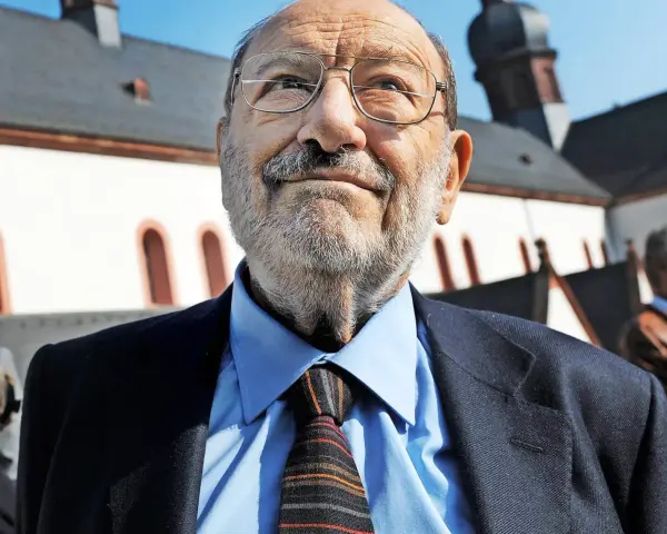 Porträt eines älteren Mannes mit Brille, Schnurrbart und Bart, der einen Anzug und eine Krawatte trägt.